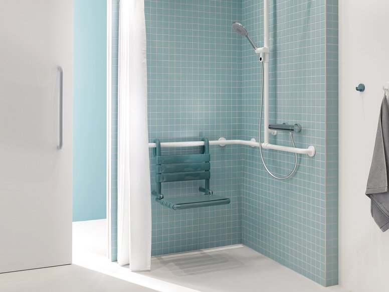 Salle de bains pour patients avec HEWI Série 477 Espace douche d'une salle de bain de patient en bleu et blanc avec vue à travers une porte coulissante