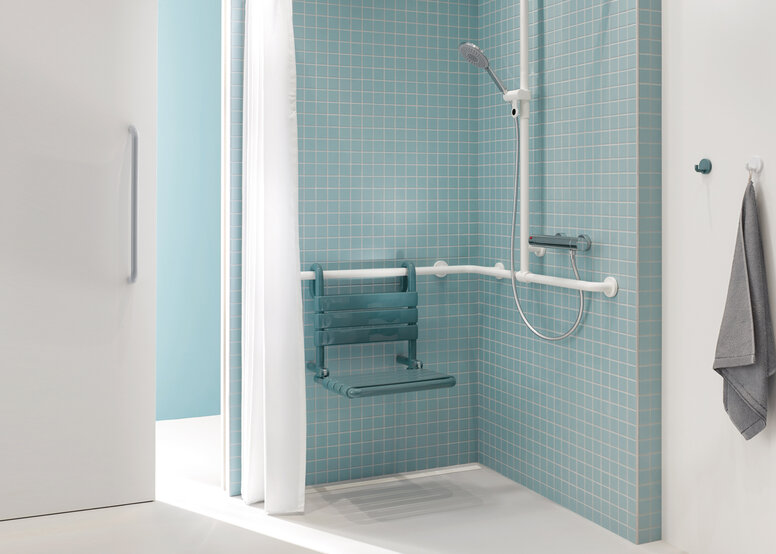 Salle de bains pour patients avec HEWI Série 477 Espace douche d'une salle de bain de patient en bleu et blanc avec vue à travers une porte coulissante