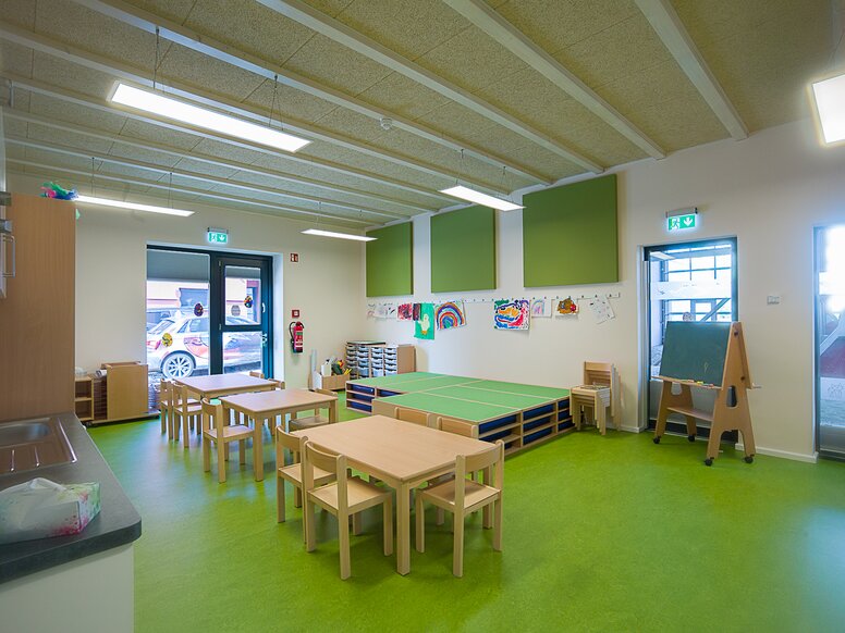 Group room of the daycare center "In der Kammgarnspinnerei" Group room of a daycare center with green floor and wooden tables and chairs